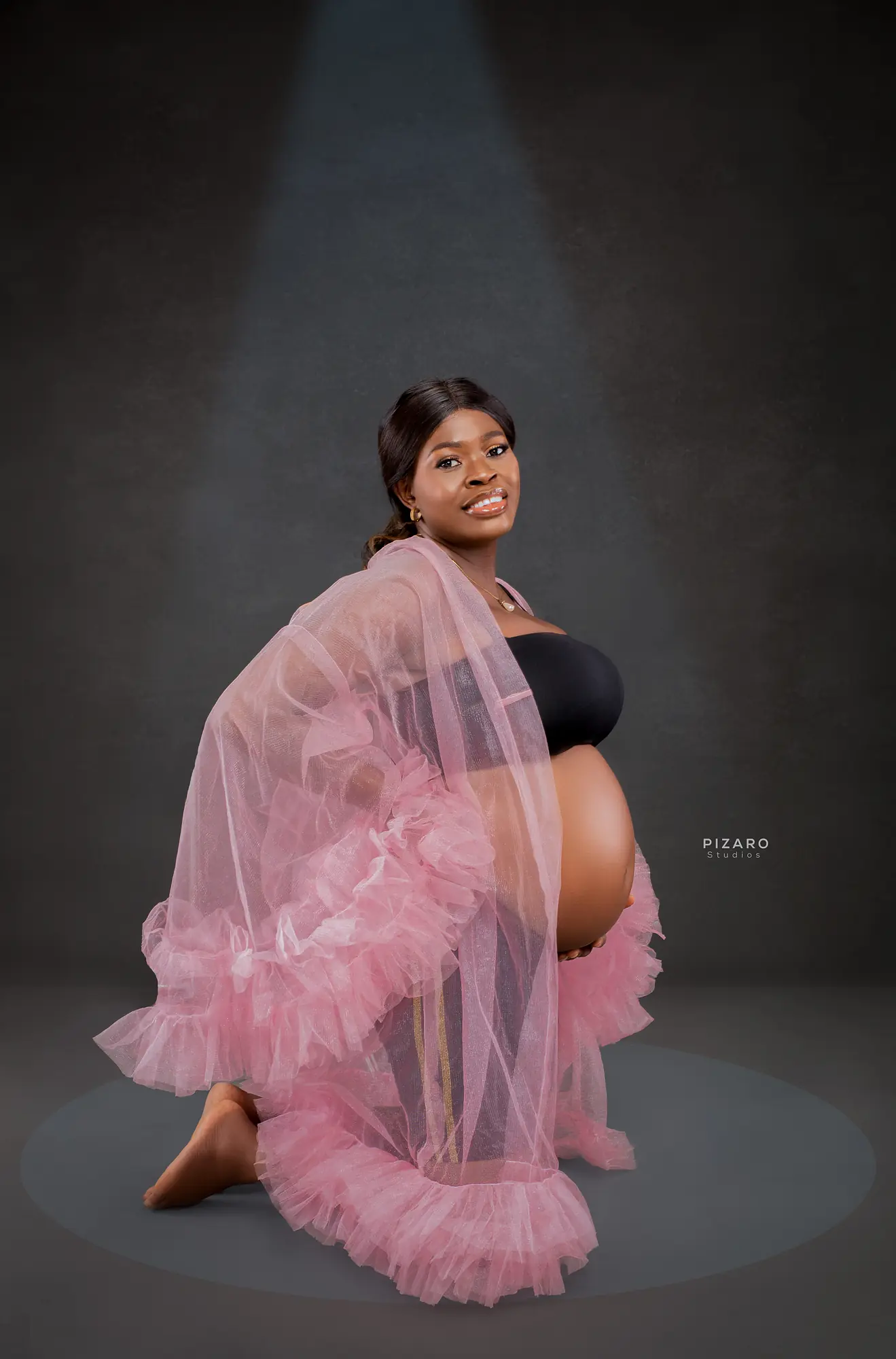 Pizaro Studios maternity session — kneeling portrait in pink tulle under a spotlight